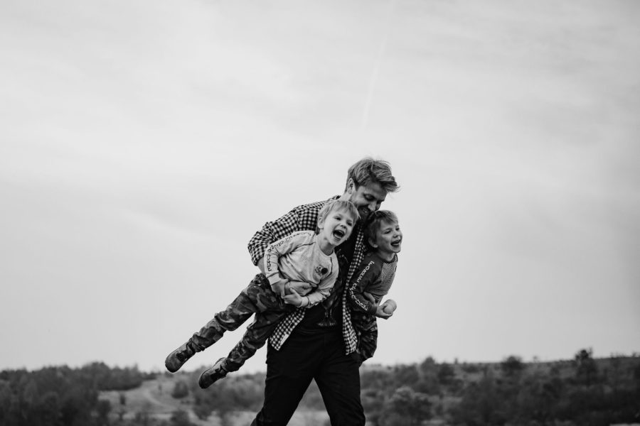 Gemeni bâieți se joacă cu tatăl lor și îi cară pe sus în brațe. Fotografie de familie