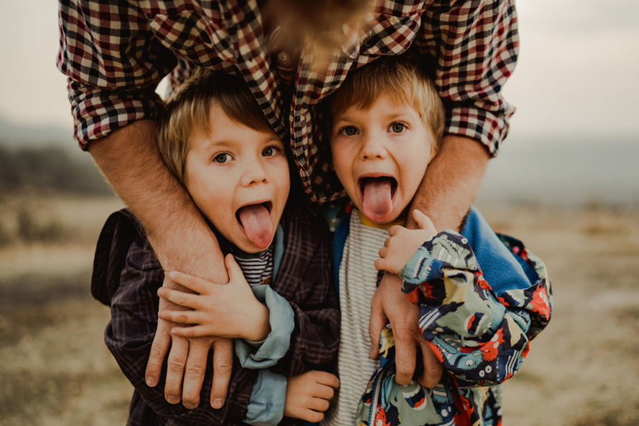 Gemeni băieți care scot limba și se prostesc în fața aparatului foto. Fotografie de familie în natură.