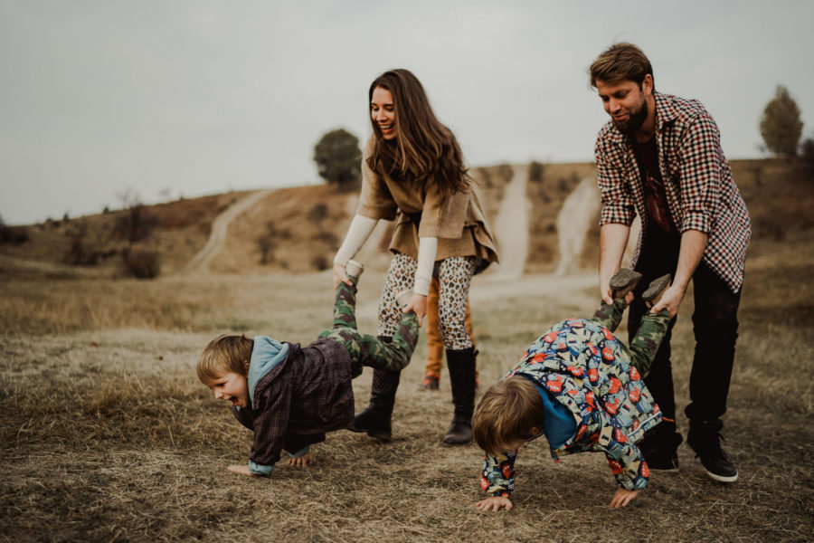Gemeni băieți se joacă cu mama sși tata de-a roaba și râd, se distrează. Fotografie de familie